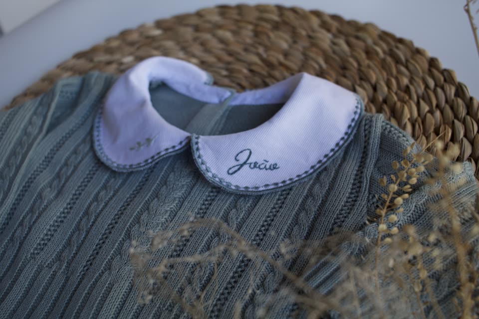 Golinha branca bordada com o nome João sobre macacão de tricô verde