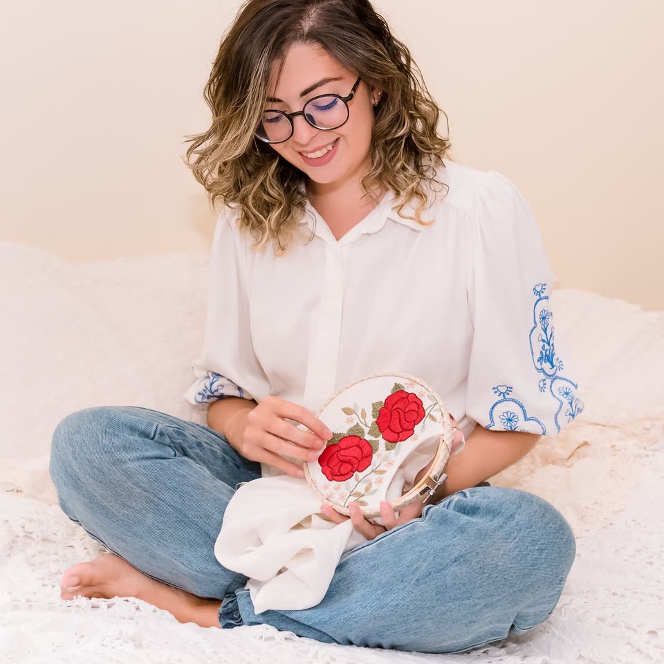 Jessyka sorrindo enquanto borda rosas vermelhas em um bastidor