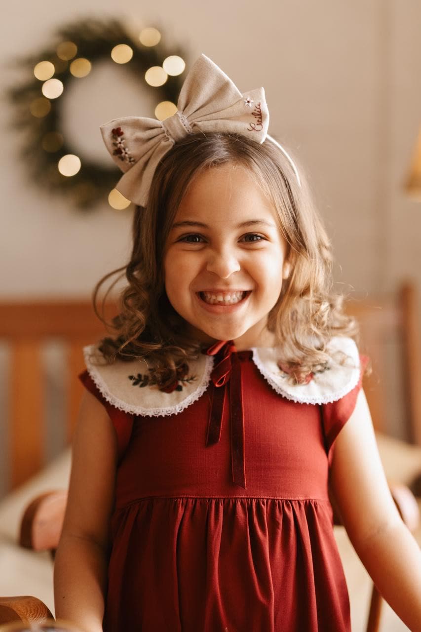 Menina sorrindo com laço de linho no cabelo e golinha bordada